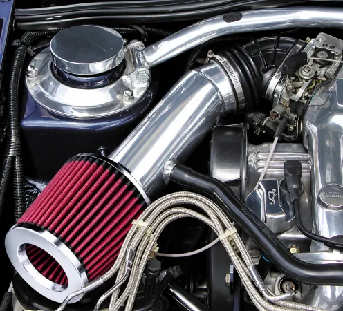Filtro aria sportivo rosso nel vano motore, collegato al blocco tramite tubo di aspirazione aria fredda (Cold Air Intake) argento lucido. Tra componenti argentati, tubi neri e cavi intrecciati, spicca.