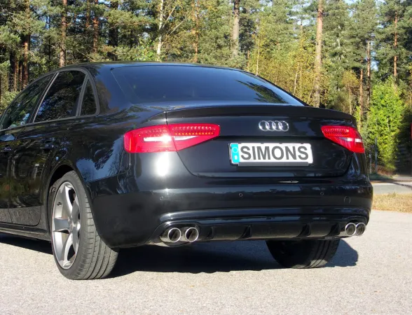 Vista posteriore di un'Audi A4 nera con scarico sportivo duplex Simons. Visibili i quattro terminali, la targa "Simons" e le luci posteriori. L'auto è parcheggiata su una strada davanti a degli alberi.